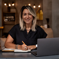 Mujer sonriente trabajando en una laptop en un ambiente acogedor con iluminación cálida.